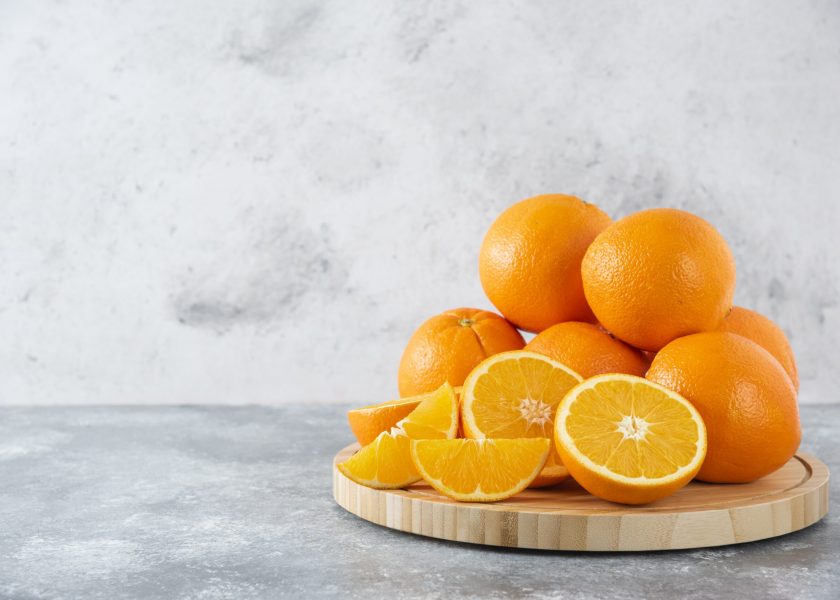 A wooden board full of juicy slices of orange fruit on stone background